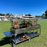 Open Fire Grill Tagwood BBQ24SS Double Argentine Santa Maria Grill 304 SS - Shared firebox - Height-adjustable grates - Interchangeable griddle -Meat hooks - Foldable side table and 6 heavy-duty swivel casters - PRE-ORDER